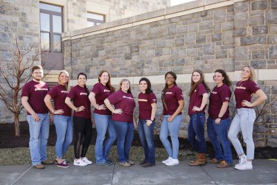 The ten  2018-219 student dairy ambassadors in maroon @vtdairyscience shirts and blue jeans posing in front of a hokie stone facade.